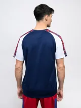 Remera de fútbol Umbro del Club Nacional de Football, modelo Pro Training Active. Diseño con estampado abstracto en blanco, rojo y azul, con mangas raglán azul marino y escudo del club en el pecho.