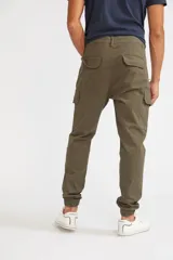 Pantalón cargo de corte slim, color verde oliva, con bolsillos laterales tipo cargo, cierre frontal con botón y puños elásticos en los tobillos.