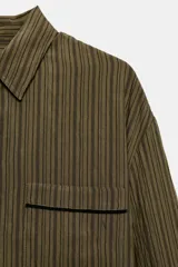 Camisa fluida de mujer de la ZW Collection de Zara, confeccionada en mezcla de viscosa, con diseño a rayas en tonos verde militar y marrón oscuro. Presenta cuello solapa, manga larga con puños anchos terminados en ribete negro a contraste, bolsillo de parche en el pecho con ribete a juego, bajo redondeado y cierre frontal con botones oscuros.