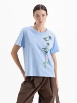 Remera de algodón con cuello redondo y mangas cortas. Presenta un diseño estampado y bordado de flores y un corazón en el frente.