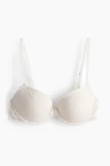 Soutien push-up color beige de punto acanalado, con copas acolchadas, aros, breteles ajustables y cierre de corchetes en la espalda. Presenta detalles de encaje en el borde superior de las copas y un pequeño lazo en el centro.