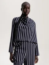 Blusa de poliéster azul marino con estampado de rayas verticales blancas. Tiene cuello abullonado y mangas largas.