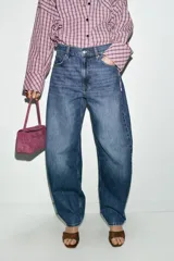 Jeans de tiro alto con diseño barrel, caracterizado por una silueta curvada y holgada en la zona de los muslos y rodillas, estrechándose hacia el tobillo. Cuenta con cinco bolsillos y cierre frontal con cremallera y botón.