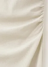 Vestido midi color beige de silueta slim, sin mangas y con cuello barca. Presenta frunces sutiles en los laterales de la cintura.