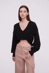 Sweater negro de tejido de punto con diseño cruzado en el frente, escote en V profundo y mangas largas con puños ajustados.