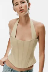 Top estilo corsé color beige, con escote recto, cuello halter y bajo asimétrico. Presenta costuras estructuradas frontales.
