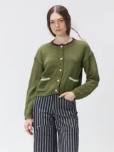 Cardigan de algodón grueso en color rojo, con cuello redondo y cierre frontal de botones grandes. Presenta bolsillos cuadrados en el bajo con detalles de pelo sintético en los bordes y logo bordado en uno de ellos. Posee puños y ruedo elastizados con diseño holgado.