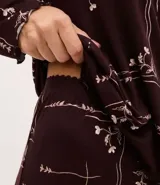 Pijama de dos piezas estilo americano en color bordó con estampado floral. La blusa es de manga larga, con cuello solapa, cierre frontal abotonado y terminaciones onduladas en los puños. El pantalón es largo y de corte recto.