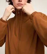 Campera rompevientos color verde oliva con capucha ajustable con cordón, cierre frontal con cremallera, bolsillos laterales con cremallera, puños con elástico y forro interior. Ligera y versátil, ideal para proteger del viento y la lluvia ligera.