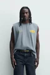 Musculosa de corte relajado con efecto lavado, cuello redondo y sisas amplias. Presenta estampados gráficos en color amarillo en el frente y acabados irregulares que le otorgan una apariencia única.