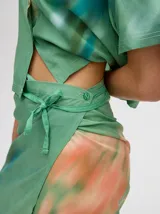 Falda midi tipo pareo color verde con estampado estilo tie-dye en tonos azul, naranja y blanco, con tiras ajustables en la cintura.