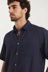 Camisa sport de manga corta, confeccionada en una mezcla de lino y algodón. Presenta cuello clásico, cierre frontal con botones de coco y un bolsillo aplicado en el pecho.
