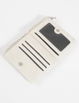 Billetera tipo flap de acabado brillante, con cierre frontal a presión y compartimento con cierre superior. Presenta un aplique metálico decorativo en la parte inferior.