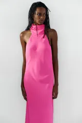 Vestido largo fucsia de cuello halter, espalda descubierta y cierre lateral con cremallera oculta en costura.