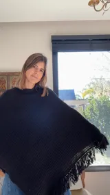 Poncho tejido en lana merino, color negro, con diseño de cuello alto y terminación de flecos en el ruedo.