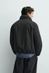 Cazadora acolchada de corte boxy fit, color negro, con cuello subido, cierre frontal de cremallera, bolsillos con solapa en la cadera y bajo con acabado elástico.