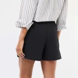 Falda pantalón de color negro con diseño asimétrico y cierre frontal con botón dorado decorativo.