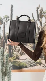 Cartera estructurada de tamaño mediano, confeccionada en símil cuero color negro. Presenta doble asa de mano, correa larga ajustable y desmontable, y un bolsillo trasero con cierre. El compartimento principal cuenta con cierre, división interna y bolsillos organizadores.