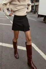 Bermuda de tiro alto color negro, con diseño de tablas frontales y detalle de eslabones metálicos dorados en la cintura. Cuenta con cierre lateral oculto.