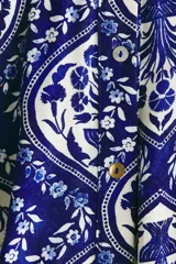 Vestido midi camisero de color azul con estampado ornamental en tonos blancos y azules. Cuenta con mangas cortas raglán, botonadura frontal completa y cinturón de la misma tela para atar en la cintura.