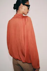 Top de punto color naranja con cuello polo, escote en V y mangas largas amplias con bajo abullonado.
