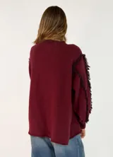 Sweater de punto color negro, con cuello redondo, mangas largas abullonadas y detalles de flecos en las costuras de los hombros y mangas.