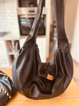 Bolso de hombro grande de cuero negro, con correa ancha y bolsillo interno con cierre.