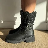 Bota de caña media confeccionada en cuero vacuno, con interior forrado en corderito. Presenta una suela de goma tipo track con plataforma y detalle de tira con hebilla metálica en la parte superior de la caña.
