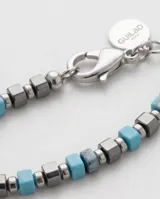 Pulsera elástica compuesta por una alternancia de cuentas de piedra natural en color turquesa y cuentas metálicas de acero en forma cúbica.