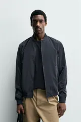 Cazadora bomber ligera de tejido técnico color verde oliva, con cuello, puños y bajo en rib elástico. Presenta cierre frontal de cremallera y bolsillos de vivo en la cadera.