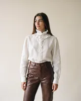 Camisa de lino blanca con cuello alto fruncido tipo gola, lazo decorativo y mangas largas.