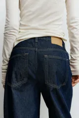 Jean de tiro alto con corte baggy, confeccionado en denim de algodón. Presenta diseño de cinco bolsillos, cierre frontal con botón y silueta de pierna curva con volumen en la cadera.