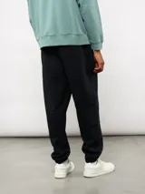 Pantalón jogger de felpa color negro, con cintura elástica, puños en los tobillos y etiqueta con el logo de la marca en la parte frontal.