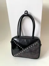Cartera rígida negra con detalles en rojo y tachas plateadas. Tiene herrajes y cierre metálico plateado marca YKK, asa fina para llevar al hombro o en la mano y correa larga extra regulable. El interior es forrado, tiene un bolsillo con cierre enmarcado en cuero, y un segundo bolsillo plaqué.