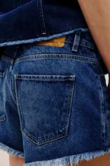 Short de denim azul medio con diseño de cinco bolsillos, cierre frontal con botones y bordes desmechados en el ruedo.