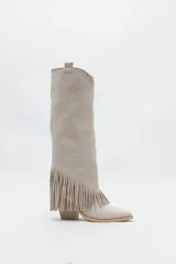 Bota texana de caña alta color beige confeccionada en gamuza, con punta fina, taco cuadrado de madera y detalle de flecos laterales. 