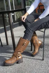Bota de cuero color marrón, de caña alta con hebillas decorativas y cierre lateral.