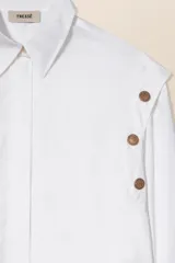 Camisa blanca de corte ancho con botones a presión ocultos y sisas decoradas con botones a presión dorados con forma de sol.