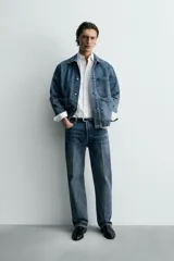 Cazadora de denim de algodón, color azul medio lavado, con cuello solapa, manga larga y cierre frontal de botonadura. Presenta cuatro bolsillos de plastrón con tapa y botón en el frente (dos en el pecho y dos a la altura de la cadera).