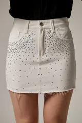Minifalda de jean blanca con tachas y strass aplicados en la parte delantera, tiro alto y ruedo desmechado.