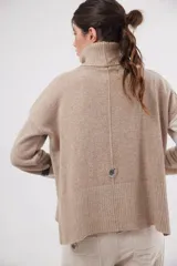 Polera de calce relajado con cuello alto, confeccionada en lana. Presenta un diseño bicolor con cuerpo en gris claro y mangas con estampado jacquard de arabescos en tonos tierra y negro. Incluye detalle de costura central vertical en el frente.