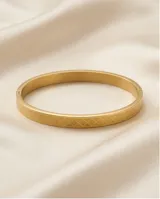 Pulsera tipo esclava rígida de acero con baño de oro, con diseño grabado de textura geométrica en forma de rombos.