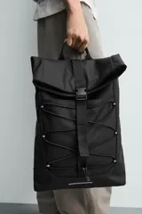 Mochila técnica de acabado engomado en color negro. Presenta un diseño de solapa con cierre de hebilla de liberación rápida y un sistema de cordones elásticos frontales. Incluye compartimento para dispositivos electrónicos, espalda acolchada y correas ajustables.
