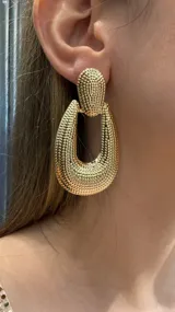 Caravanas colgantes de diseño geométrico ovalado con textura granulada en acabado dorado brillante.