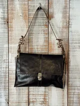 Cartera de cuero negro con acabado brillante, diseño rectangular con solapa frontal y cierre metálico a presión. Presenta una correa larga ajustable con detalles decorativos de tiras entrelazadas en los extremos.