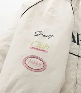 Campera bomber de microfibra color beige con estampado frontal de lettering 'PARIS 1985'. Presenta cierre frontal con cremallera, cuello alto, bolsillos funcionales y puños y ruedo ajustados con elástico.