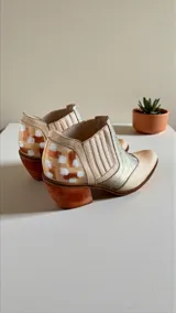 Botas cortas de cuero color natural con inserciones de cuero plateado con textura de cocodrilo en el empeine, paneles laterales elásticos y detalles pintados a mano en el talón. Cuenta con taco de madera de 5 cm.