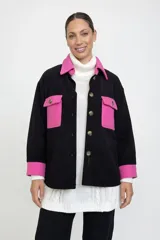 Sobre camisa de corte oversize en color negro con detalles en fucsia en cuello, bolsillos frontales y puños. Presenta cierre frontal con botones y diseño de dos tonos.