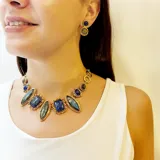 Caravanas artesanales de bronce con dos piedras naturales engarzadas en disposición vertical, una de color azul y otra gris. Presentan un acabado rústico con detalles circulares y cierre de presión.