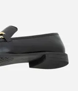 Zapato mocasín femenino de PU color negro, con punta cuadrada y detalle metálico dorado en el empeine. Tiene un tacón bajo y suela de goma.